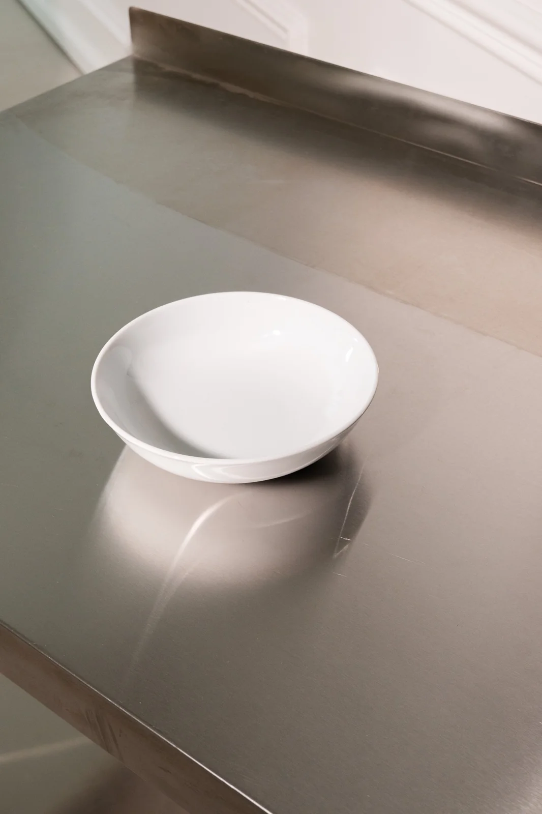 Weiße Delta-Bowlschale mit hohem Rand auf einer Edelstahlfläche. Weitere Ansicht.