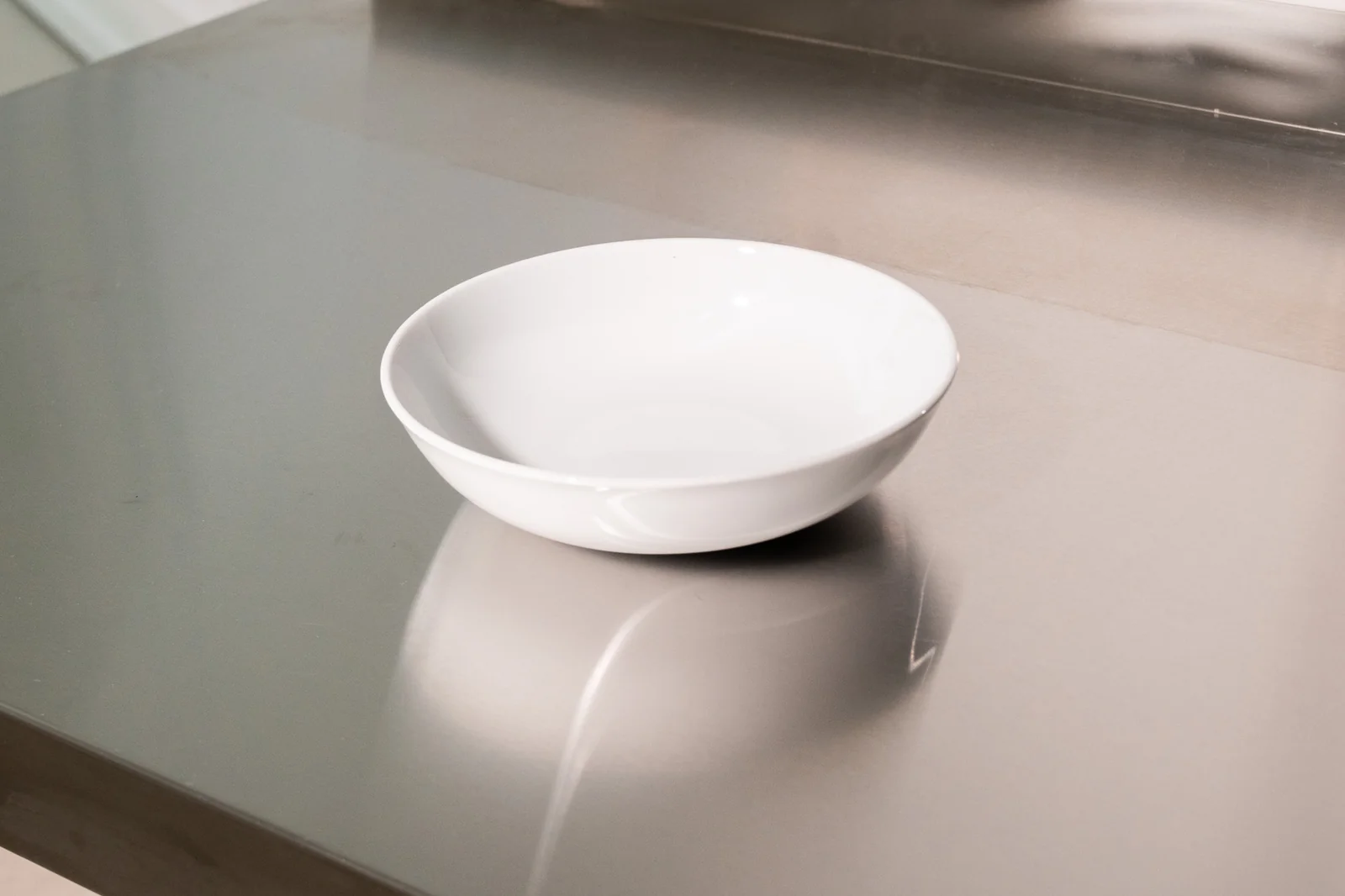 Weiße Delta-Bowlschale mit hohem Rand auf einer Edelstahlfläche.