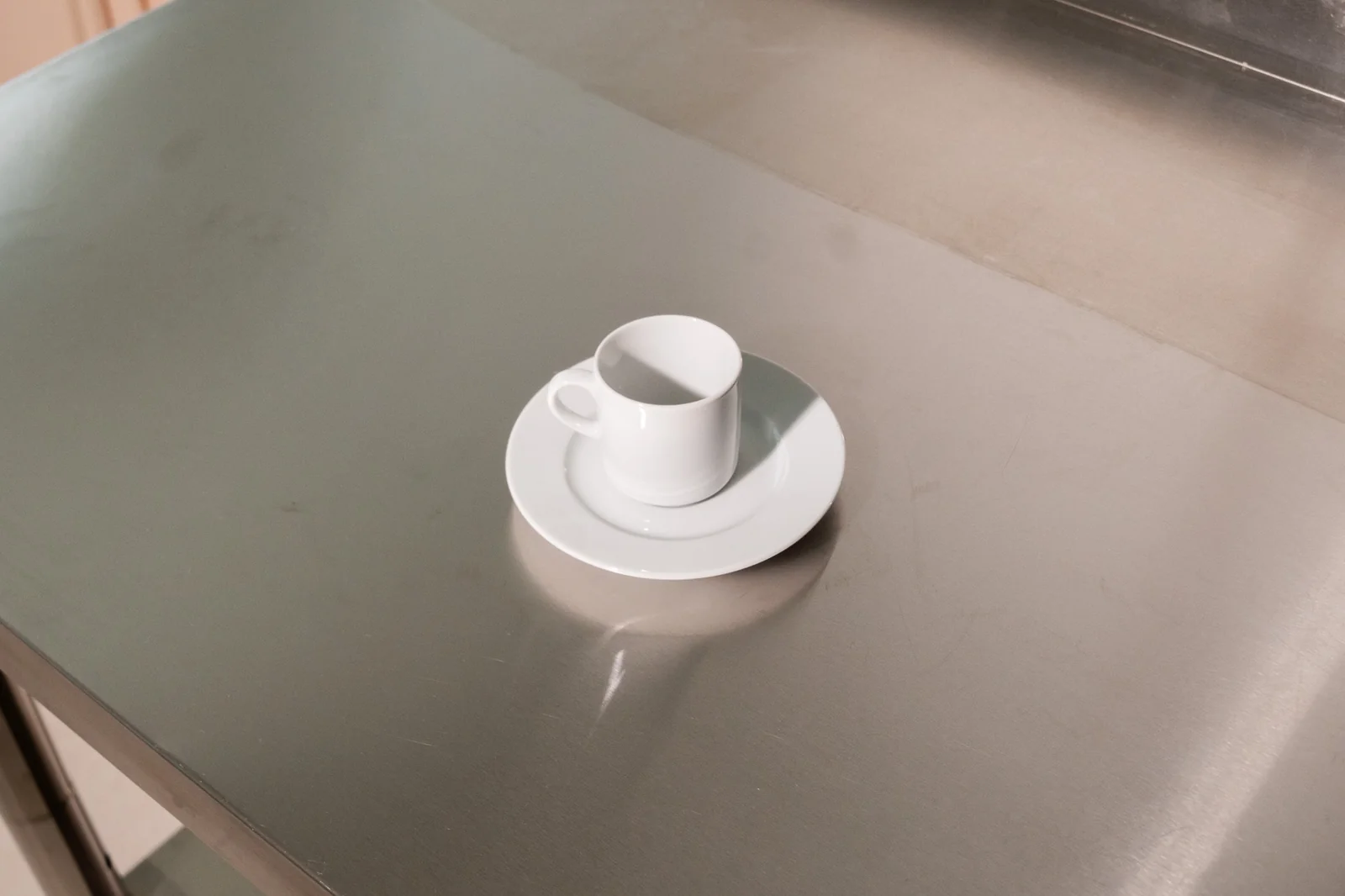 Weiße Delta-Espressotasse mit passender Untertasse auf einer Edelstahlfläche. Weitere Ansicht.