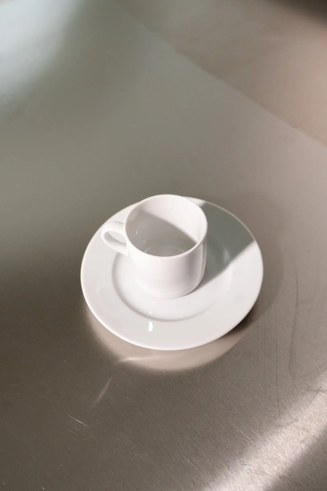 Weiße Delta-Espressotasse mit passender Untertasse auf einer Edelstahlfläche.