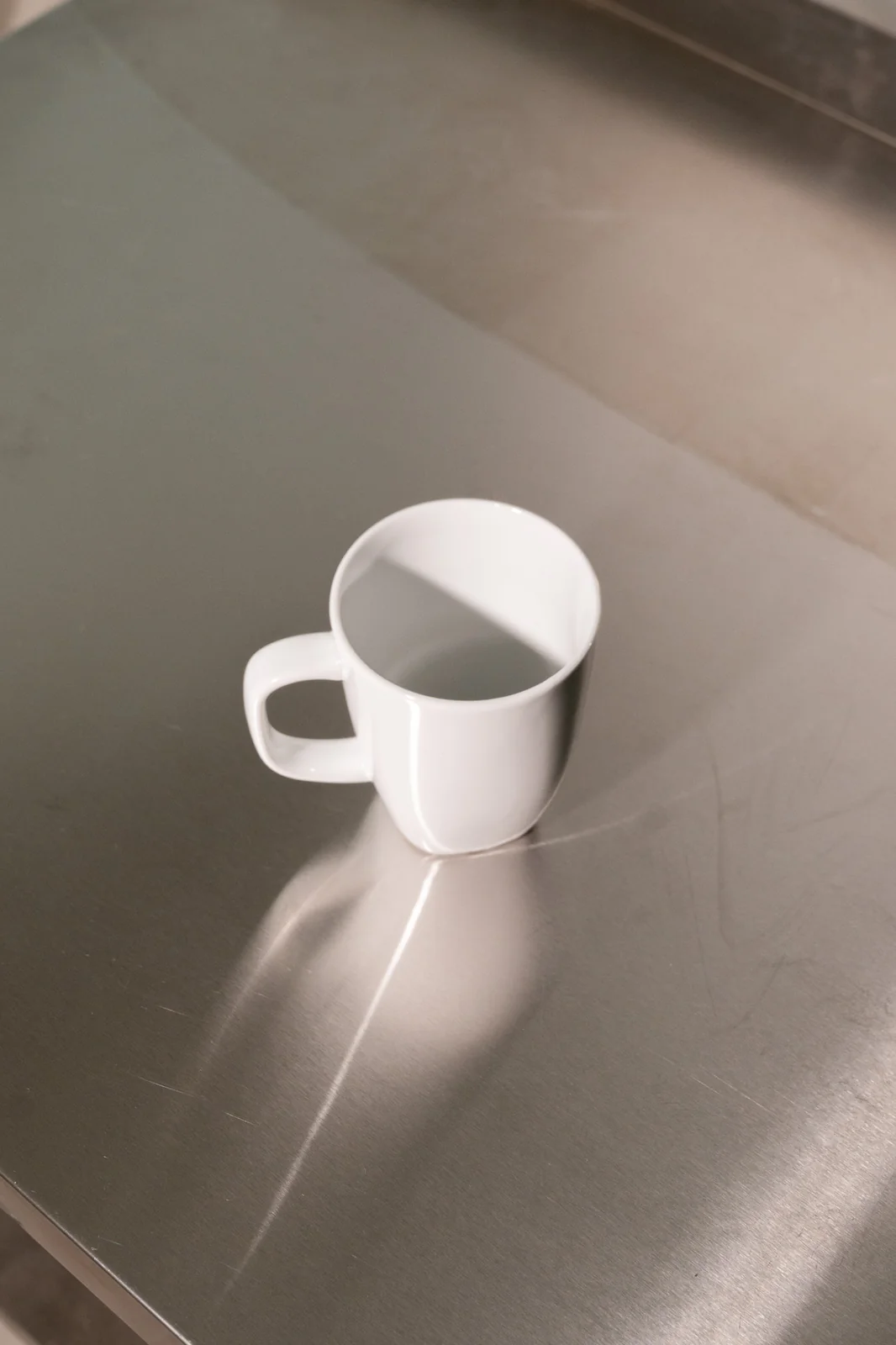 Große weiße Delta-Kaffeetasse mit eckigem Henkel auf einer Edelstahlfläche. Weitere Ansicht.