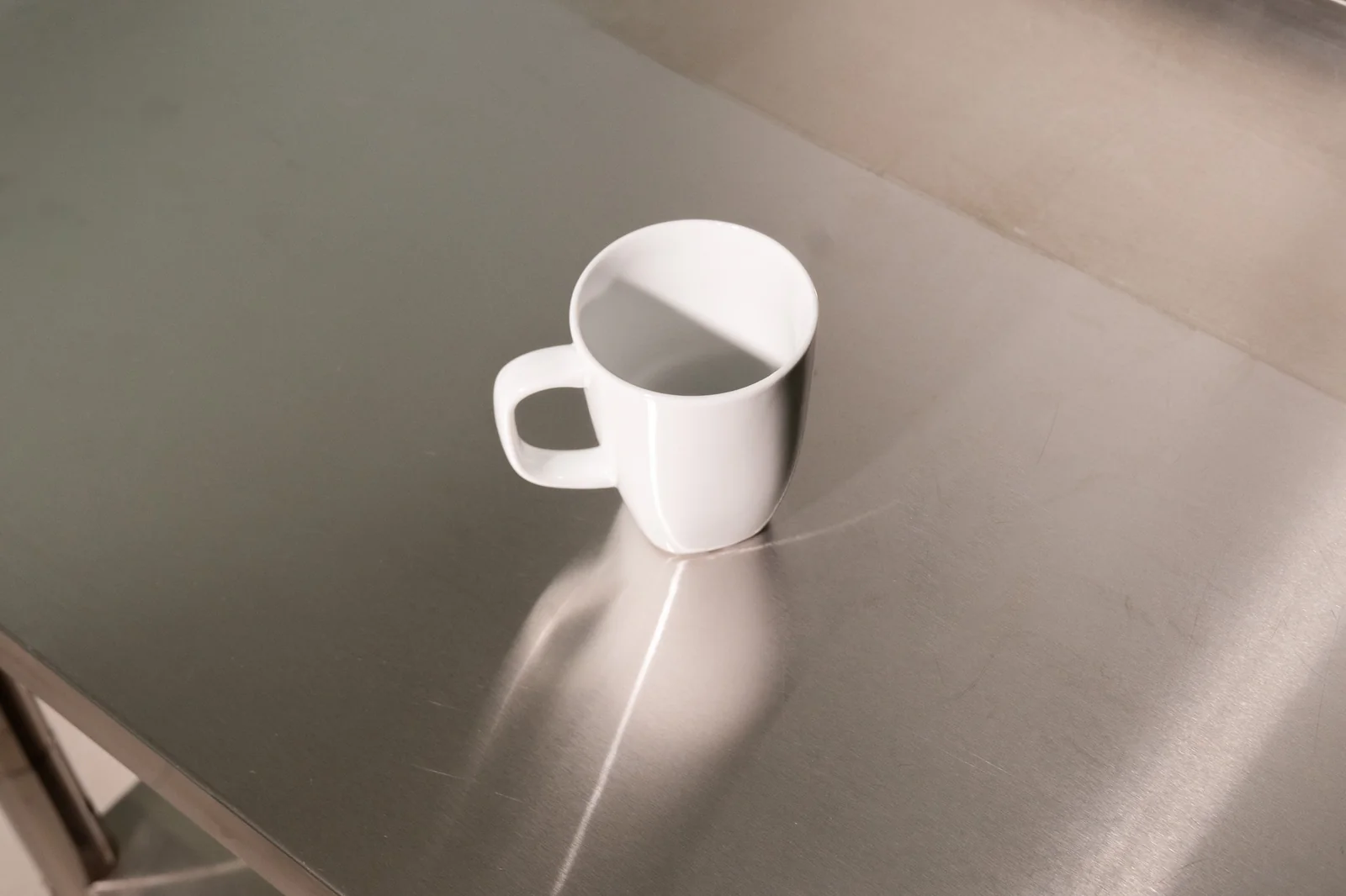 Große weiße Delta-Kaffeetasse mit eckigem Henkel auf einer Edelstahlfläche.