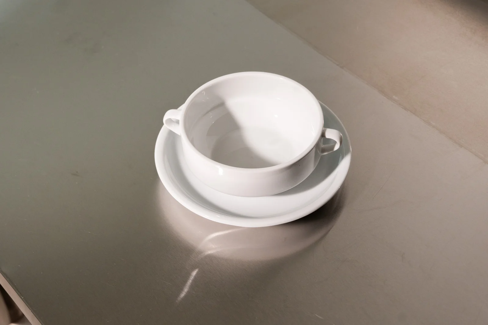 Weiße Delta-Suppentasse mit zwei Henkeln und passender Untertasse.